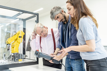 Colleagues watching woman programming robot arm with digital control