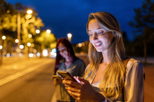 Smiling Woman Using Smart Phone With Friend In Background