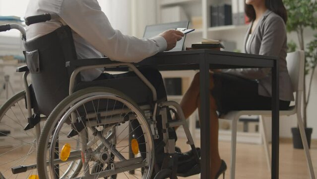 Company boss in wheelchair interviewing young woman for job, business handshake