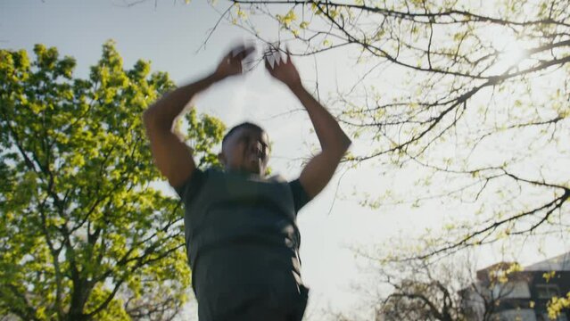 Young black man in sports clothing doing burpees at during fitness training in park
