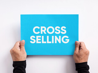 Male hand holding a blue paper with the word cross selling. Selling different products or services to an existing customer.
