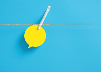 Blank yellow speech bubble attached on a clothesline with a clothespin on blue background.