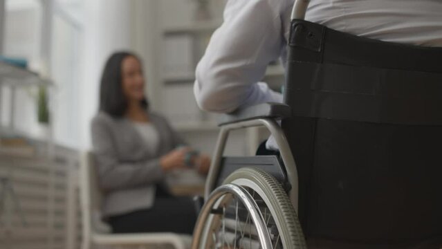 Man in wheelchair having casual conversation with office colleague, lunch break