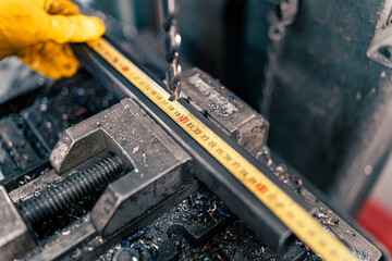 Close-up of a metal bar in a clamp and a drill bit, the craftsman measures exactly where he needs to drill