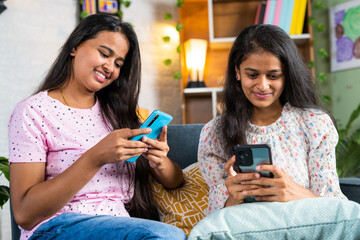 siblings busy using mobile phone while sitting on sofa at home - concept of social media addiction, cyberspace and relationship.