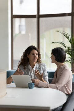 Two Happy Engaged Business Professionals Women Brainstorming On Online Project At Laptop, Speaking, Discussing Creative Ideas, Plan, Strategy, Task, Chatting At Work Desk In Office