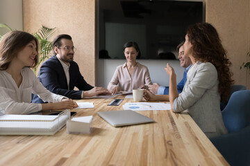 Millennial business team and senior female leader engaged in teamwork discussing statistic reports, marketing strategy at meeting table, talking, smiling, offering ideas for startup in boardroom