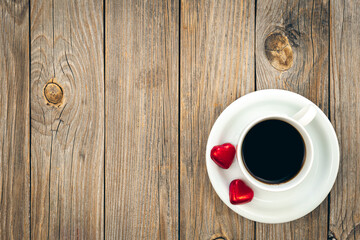 A cup of coffee and heart-shaped chocolates on a wooden background, top view.