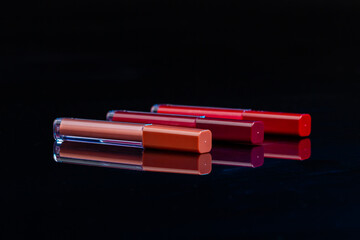 Three lip gloss sticks with closed caps. Reflective surface and black background.