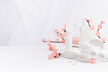 Cosmetic products in white bottles, branch of spring pink sakura flowers, toiletry for hygiene, cleansing, body care in soft light white interior in geometric modern asian style, copy space.