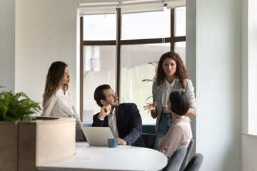 Diverse team meeting at work desk with laptop, listening to serious young female boss. Business...