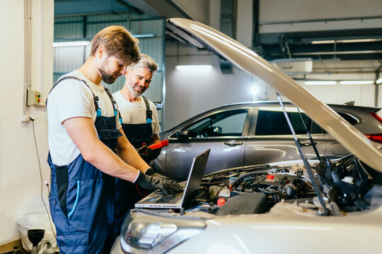 Two serviceman team of worker making car diagnostics with laptop in a workshop