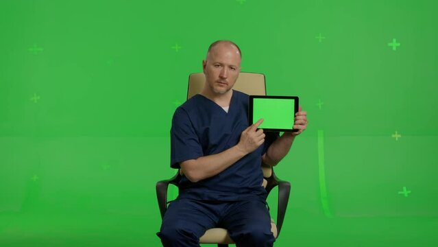 medical doctor sitting in an office chair showing promotional information on a green screen tablet