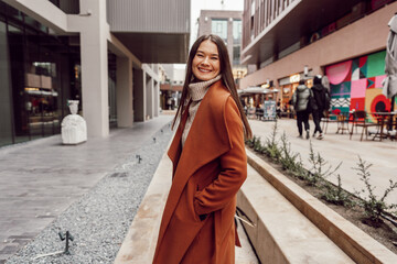 Young beautiful woman in brown coat walking on the autumn street.