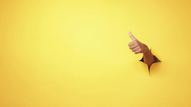 Like gesture. Perfect choice. Approval yes. Female hand recommending showing thumb up in yellow breakthrough hole ripped paper wall on advertising copy space background.