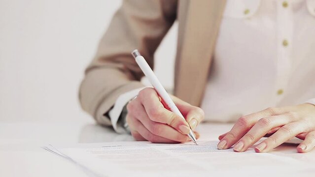 Hands of a Caucasian businesswoman writing on a document.