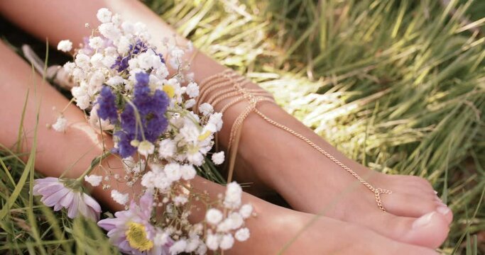 Cropped Overhead Shot Of A Girl's Feet Resting In Lush Green Grass With Fresh Flowers And Delicate Foot Jewellery