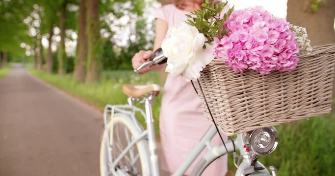 Fresh spring flowers in the woven basket of a classic vintage style bicycle being pushed in a park by a woman, Panning in Slow Motion