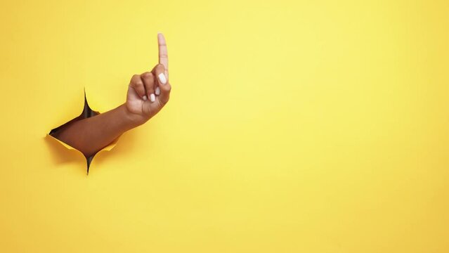 Finger wag. Restriction sign. Rejection signal. Female hand warning no in yellow breakthrough hole ripped paper wall copy space background.