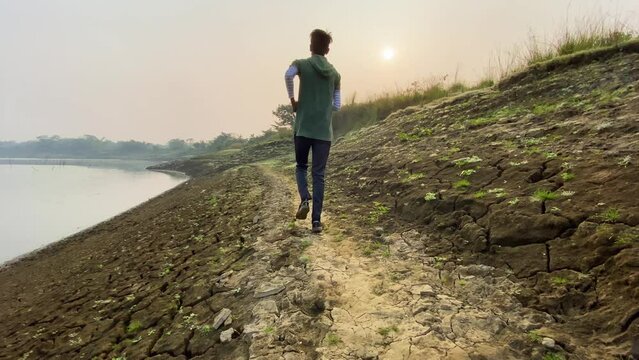 Rear view of man jogging by river, heavy drought in Bangladesh, slowmo, day