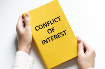 conflict of interest inscription on the cover of a yellow notebook in the hands of a man on a white background. business concept