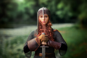 Beautiful red haired girl in metal medieval armor dress with sword standing in warlike pose and looking at camera with fearless. Fairy tale story about warrior . Warm art work. - obrazy, fototapety, plakaty