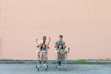 Multiethnic group of happy playful friends playing and having fun with supermaket shopping carts
