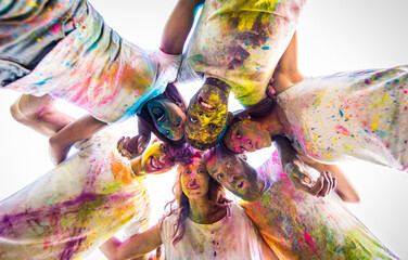 Multiethnic group of happy playful friends playing and having fun with holi colorful powder at the park