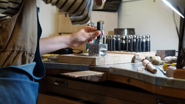 Handheld midsection of female artist hammering dapping punches on doming block at workbench in workshop