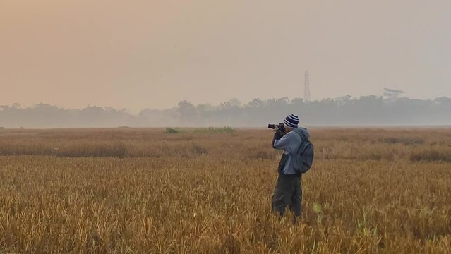 Single photographer wearing winter clothing and backpack takes pictures of field