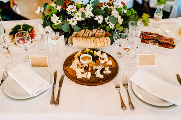 Cheese plate: Parmesan, cheddar, gouda, mozzarella and other with basil on wooden board on festive table. Tasty appetizers.