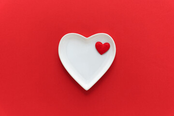 Ein weißer leerer Teller in Herzform auf einem roten Hintergrund. Valentinstag, Flat lay.