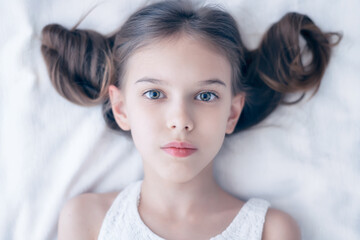 Close up shot of beautiful blonde caucasian little girl with fashionable hairstyle, lying on a bed...