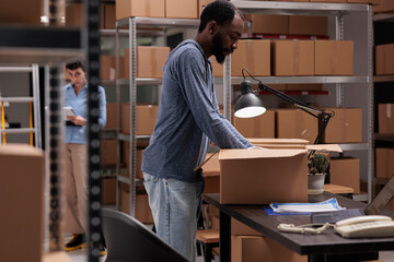 Supervisor putting customer order in cardboard box wrapping with bubble wrap for protection, checking shipping details on laptop computer before delivery package. Worker working in distribution center