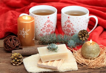 Christmas spa concept with tea and candles. Cristtmas mugs with tea, warm red blanket, handmade bar of soap and pumice stone.