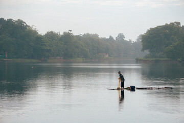Fototapeta na wymiar Fisherman is fishing with net on beautiful lake in the morning