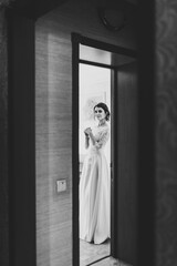 View of bride in dress through door. Beauty of bride wearing fashion wedding dress, studio photo. Attractive model. Black and white photo.