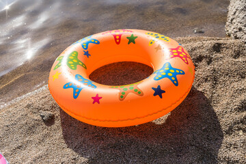 There is an orange inflatable swimming circle on the beach.