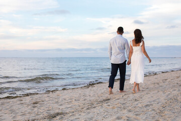 romantic couple from behind walking at beach hand in hand