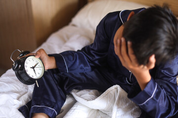Little boy is holding clock on the bed, wake up late. 