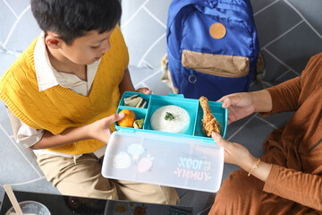 Top view mother hands giving tasty lunch in box to her son at home, prepare back to school. 