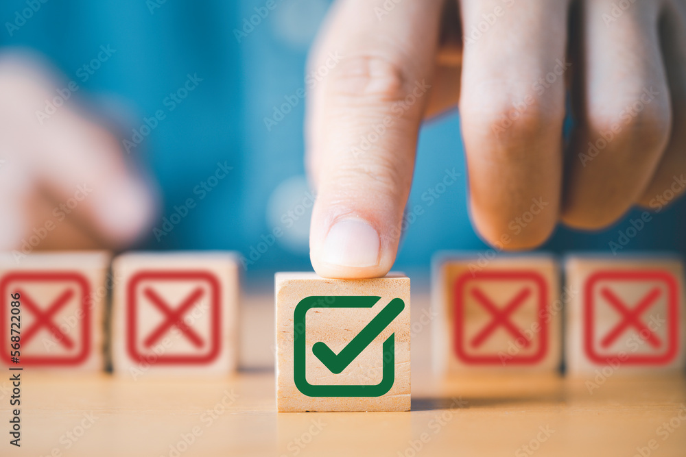 Aufkleber Hand pushing green correct sign symbol in front of Red Cross sign on wooden block cube for business proposal and document approve concept.
