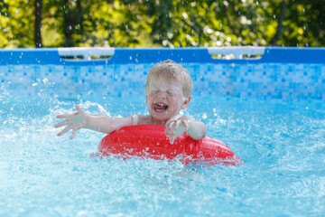 Fototapeta na wymiar blond boy in the pool splashes water and laughs