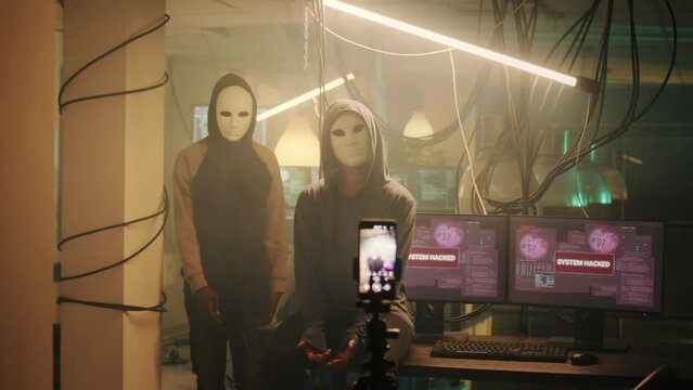 Team of anonymous people hiding identity while recording threat video for ransomware, leaking valuable government information on dark web. Hackers with masks broadcasting live montage.