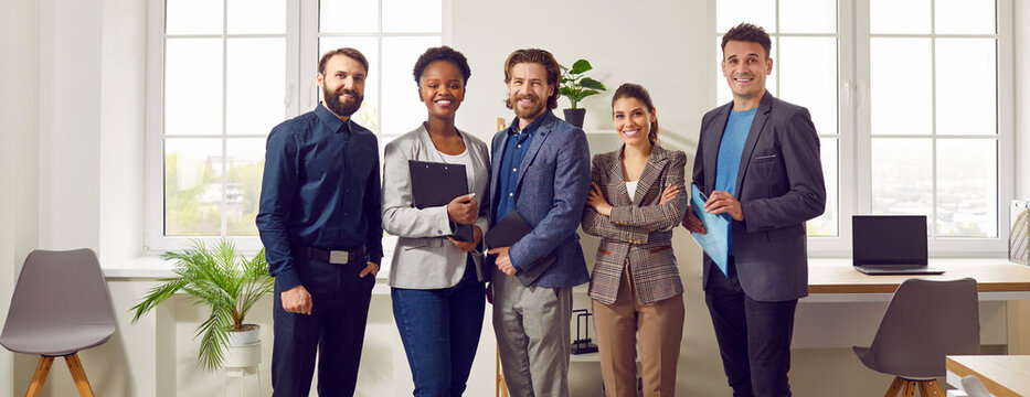 Group photo of Multi ethnic team for companys website. Colleagues stand shoulder to shoulder in their own modern office. Banner size. Successful business team smiling and posing at office.