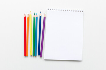 Top view Minimal design of open Notebook with colored pencils of rainbow colors on white background with blank space. Flat lay
