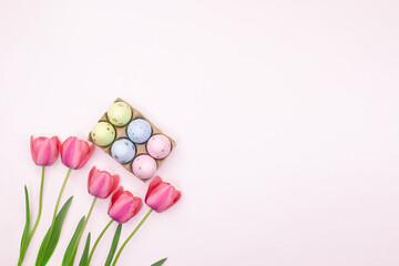 Pink tulips with basket of colored eggs in corner with place for text. Easter. Pastel background. Copy space