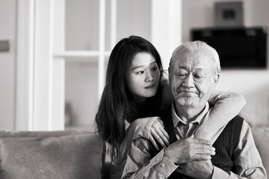 young asian adult daughter comforting heart broken senior father at home