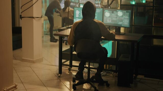 Silhouette of hacker coding encryption to plant trojan virus, looking to steal important information at night. Male thief using computer malware to hack online web network system.