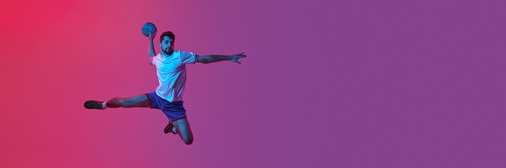 Young man, professional handball player training, playing isolated on gradient pink background in neon light. Sport, motion, championship, sportive lifestyle concept. Banner, flyer. Copy space for ad